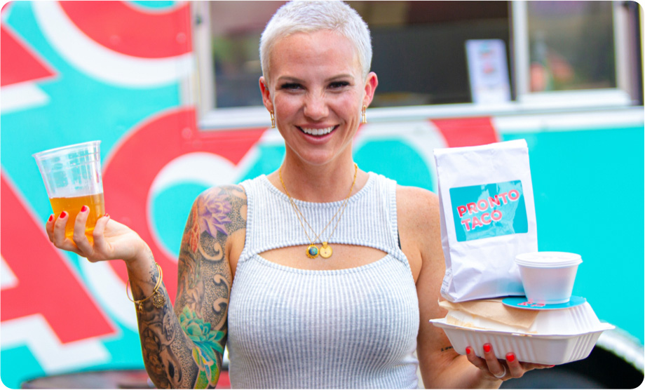 Woman with short hair holding a drink in her left hand and a taco box in her right hand